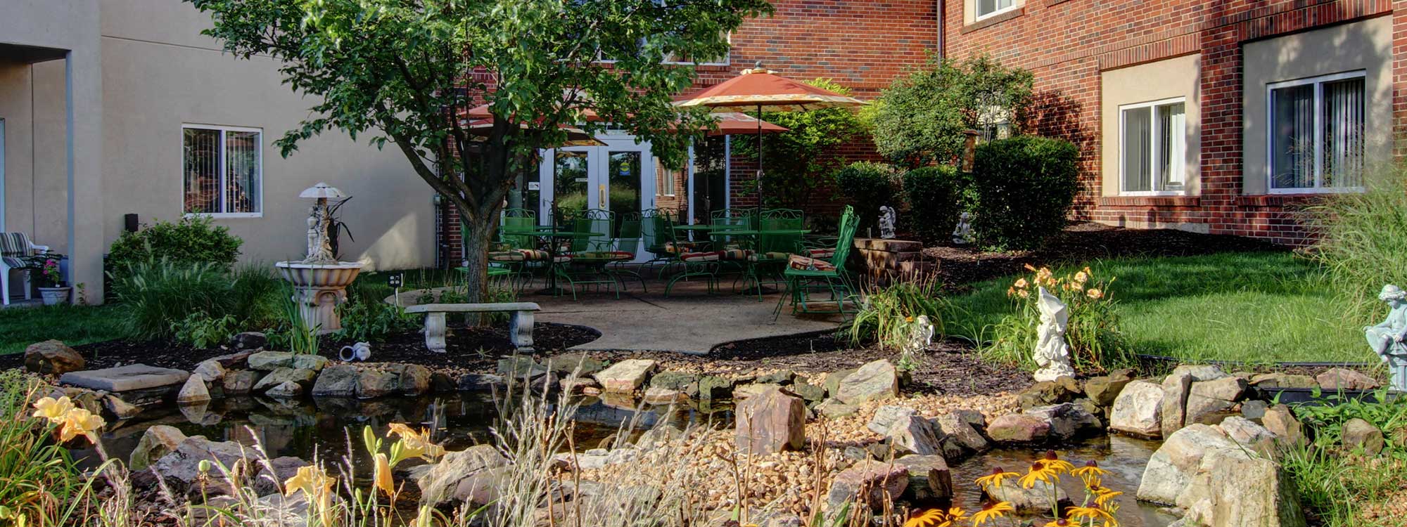 Courtyard view of the Richmond Terrace assisted living community with pond, patio seating, and landscaping in Richmond Heights, MO.